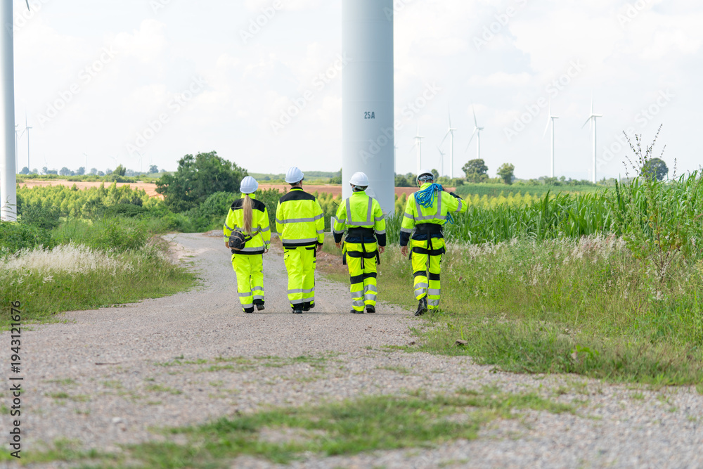 Fototapeta premium Group of diverse specialists in reflective vests and hard hats walking at wind turbine station. Industrial engineering team heading to site for clean energy production maintenance background