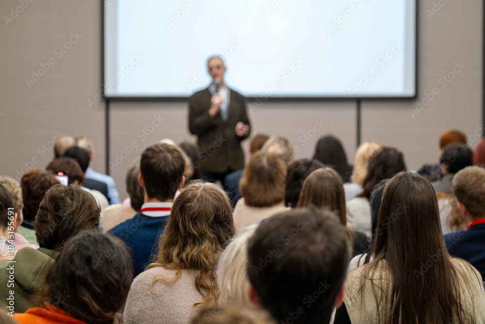 Obraz premium Conference audience listening to speaker during presentation in lecture hall, professional seminar atmosphere, focus, learning, engagement.