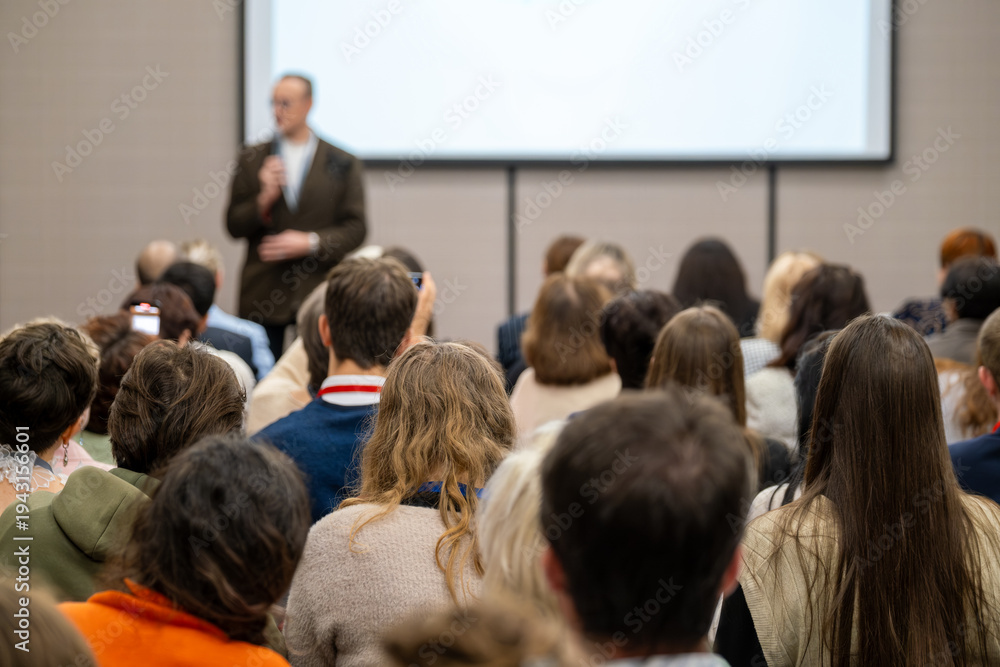 Obraz premium Audience listening to speaker at conference, people attending presentation in meeting room with projection screen.
