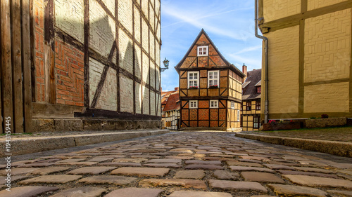 Traditional half-timbered house and narrow cobblestone street in the UNESCO World Heritage old town of Quedlinburg, Germany. Medieval German architecture under a bright blue summer sky.