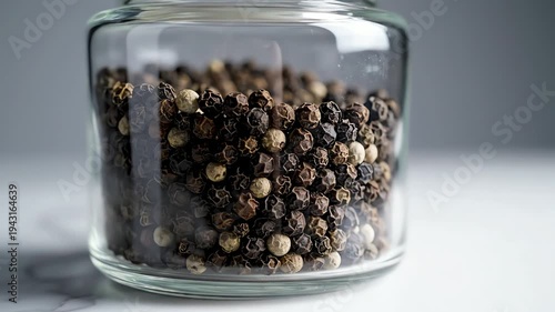 Close up of pepper grinds in a glass jar on a white surface