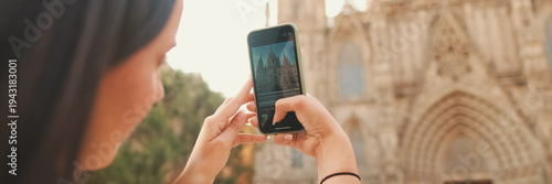 Traveler girl, with backpack on her shoulders, takes photo on mobile phone of an old building in the historical part of European city, back view. Panoramic