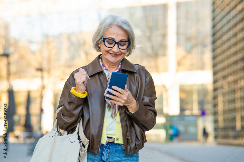 Fototapeta premium Successful senior woman celebrating a win while using a smartphone in the city