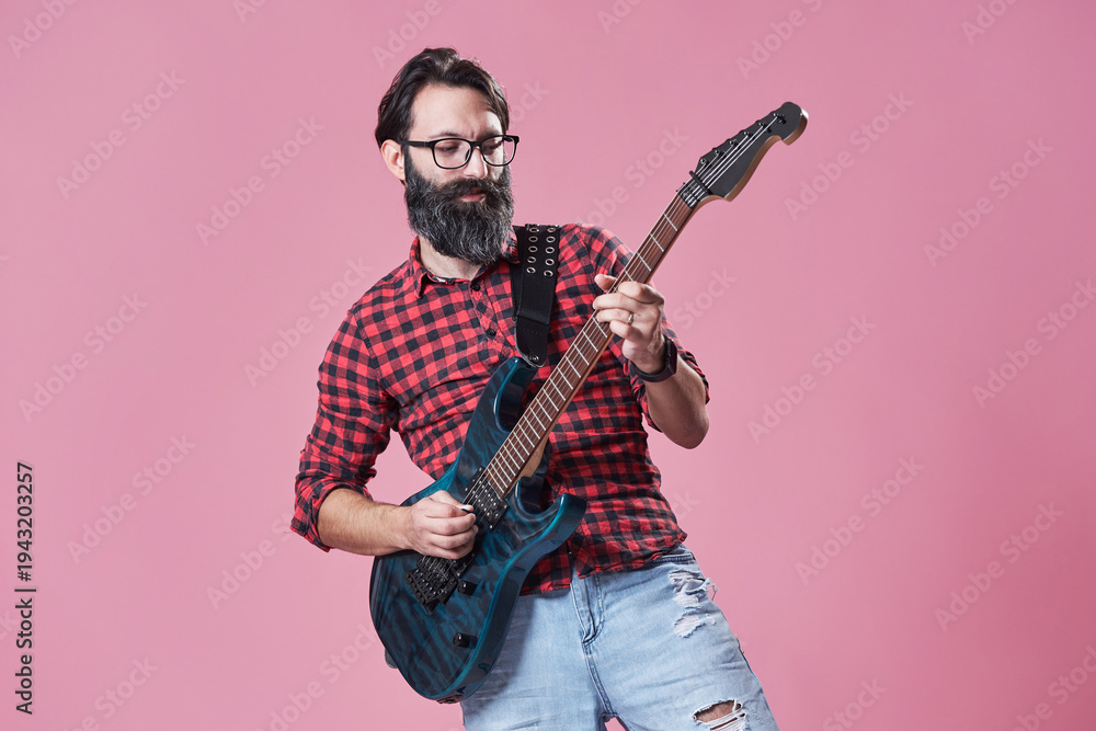 Naklejka premium Bearded man playing electric guitar in a studio against a pink b