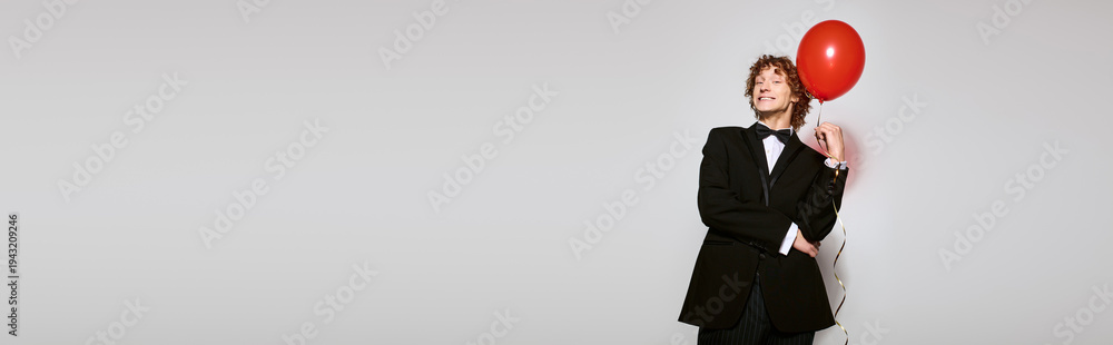 Obraz premium Curly-haired young man celebrates birthday in elegant tuxedo with a vibrant balloon