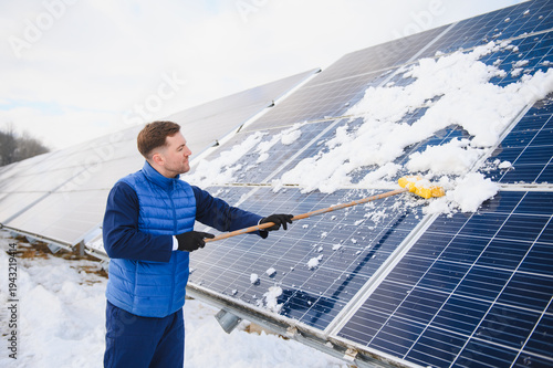 Worker cleaning snow from solar pannels in winter