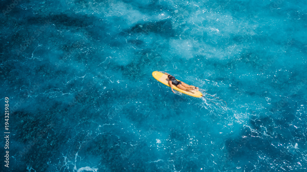 Fototapeta premium Woman on surfboard in blue sea. Drone view of surfer during surfing
