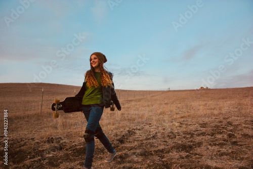 Young woman in jeans Wearing Kneepads walking in a rural landscape Carrying a Longboard, Utah, USA