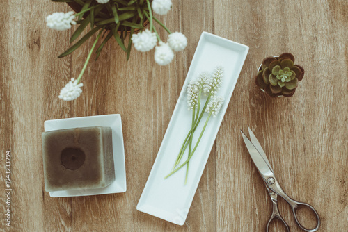 Overhead view of  a candle with a bunch of white Grape hyacinths (muscari), miniature cacti and a pair of scissors on a wooden table