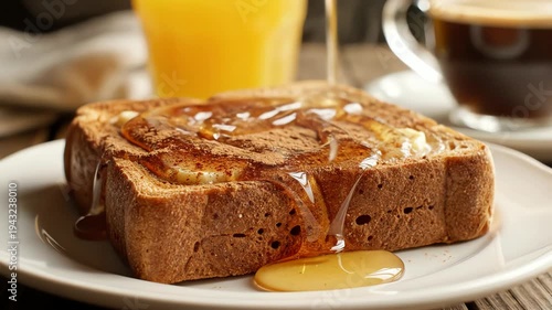 Close up of golden toast with dripping syrup on a white plate alongside a glass of orange juice and a cup of coffee
