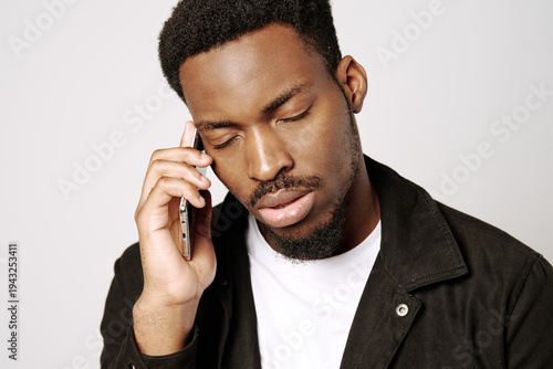 Black man experiencing communication fatigue, stress, and frustration while talking on a cellphone with eyes closed, needing a break from constant digital connection