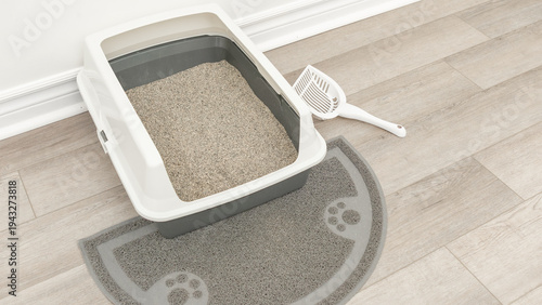 Cat litter box with gray mat and scoop placed on wooden floor, showcasing clean and organized pet care environment