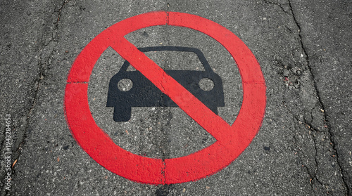 A red and black no parking symbol is painted directly onto a cracked dark asphalt road.