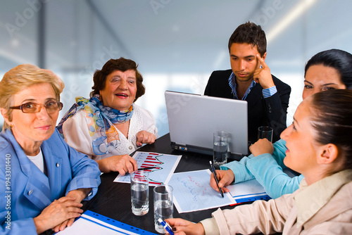 A group of people are sitting around a table with a laptop open