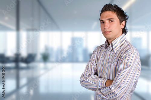 A man in a striped shirt is standing in front of a window with a city view