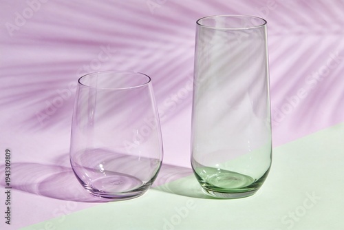 Clear glasses and green vase on light purple background with shadows