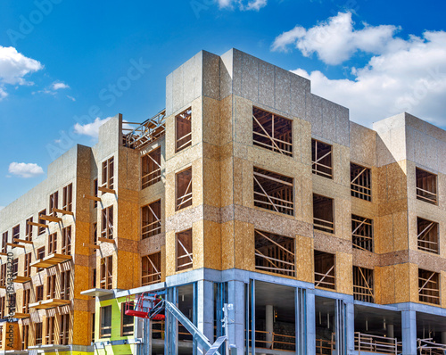 Multi-story residential building under construction using wood frame and OSB sheathing on a concrete podium base.