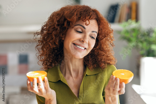 Tableau sur toile Funny mature woman holding orange slices at her face and posing at camera in the
