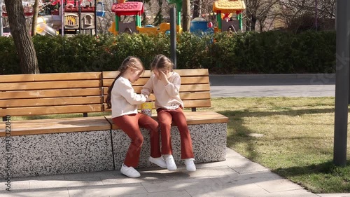 two little twin girls eating popcorn on a park bench in the spring