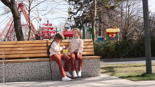 two little twin girls eating popcorn on a park bench in the spring