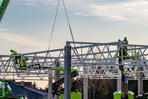 construction site with workers on an aerial lift assembling a large steel truss building framework during sunset