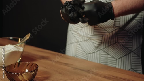 Caucasian man wearing patterned apron pulls on black gloves. Closeup of male hands and preparation for cooking in kitchen. Maintaining hygiene and sanitation while cooking and baking
