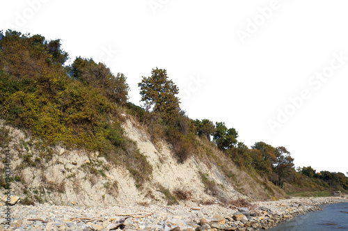 Steep coastal cliff with green foliage and rocky beach isolated on white. PNG file