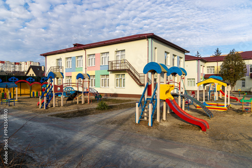 Wallpaper Mural Colorful Preschool Playground Beside Modern Kindergarten Building. Bright empty preschool playground with slides and play structures outside a modern kindergarten building under a cloudy sky. Torontodigital.ca