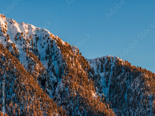Fotografi Rugged Dolomite Mountains in Italy show snow dusted peaks and pine slopes under clear blue sky