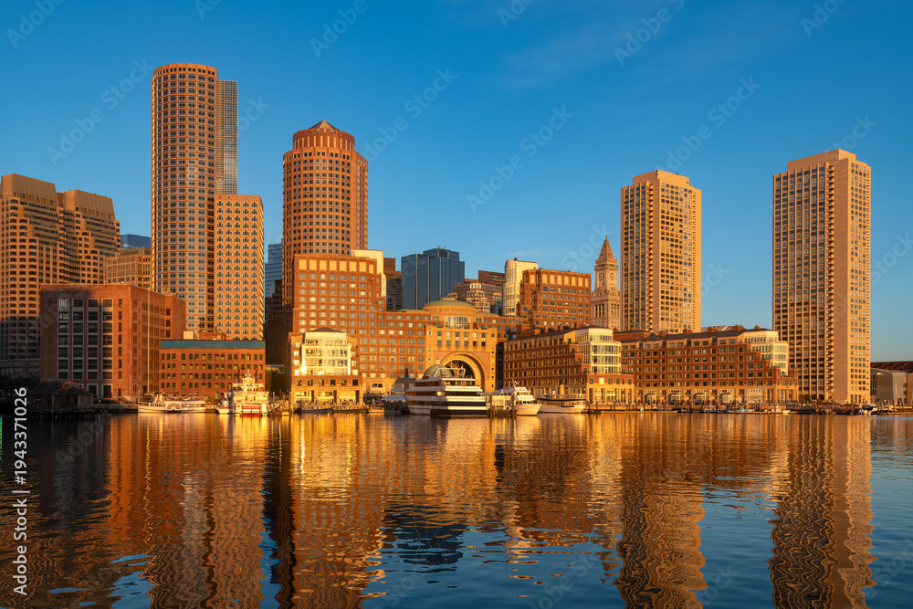 Obraz premium The Boston skyline is illuminated by the golden morning light of sunrise over the harbor.