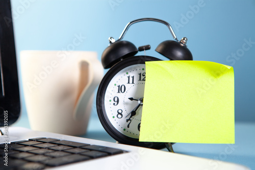 Alarm clock and sticky note with coffee cup on blue background.