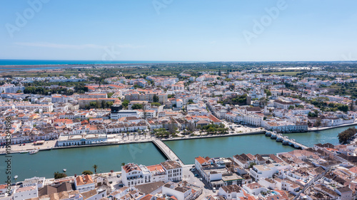 Tavira in Algarve is seen from above with traditional buildings lined along the Gilao river. The coastline and countryside can be observed in the distance