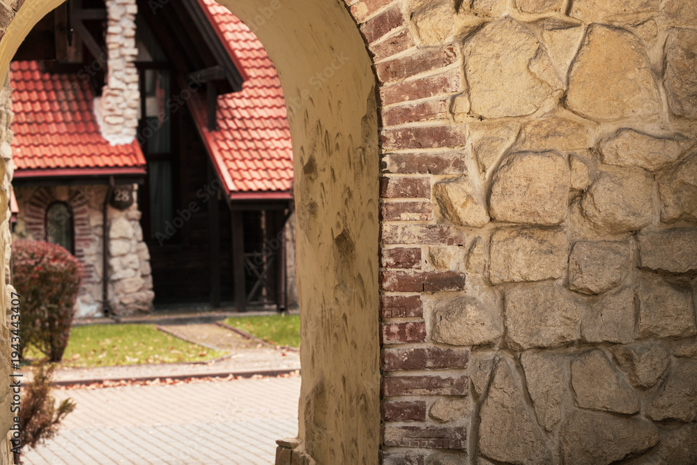 Obraz premium View through an old stone archway revealing a charming house with a red tiled roof
