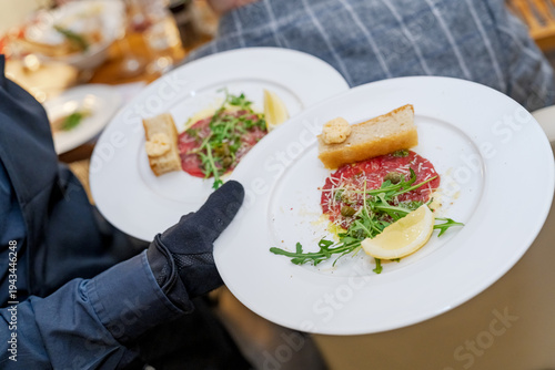 Waiter serving beef carpaccio appetizers with arugula and lemon