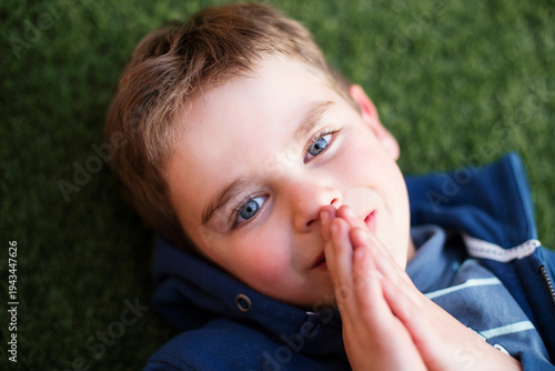 Overhead view of a young smiling boy lying on the grass praying