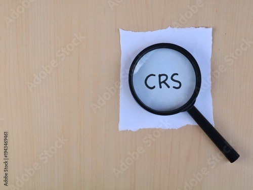 Magnifying glass over crs text on white paper on wooden background with copy space. Business concept 