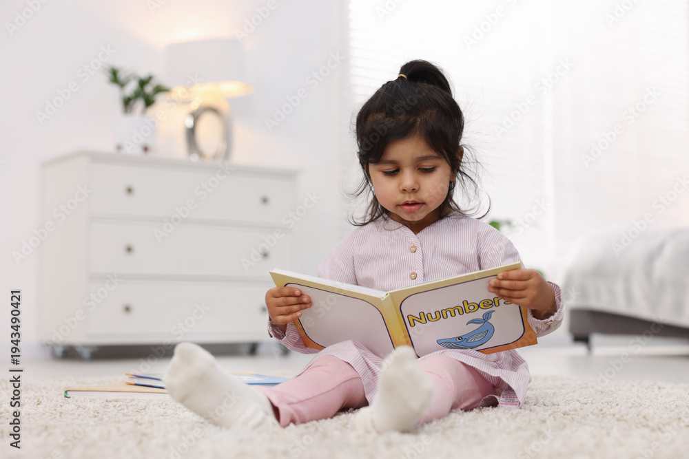 Obraz premium Cute little girl reading book on floor at home. Space for text
