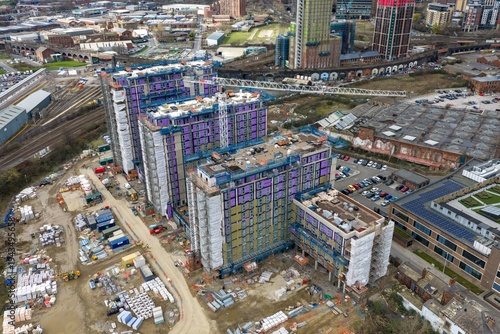 Drone aerial view of residential tower construction site in Holbeck Leeds with cranes railway tracks building materials and surrounding industrial buildings beneath cloudy sky during daytime