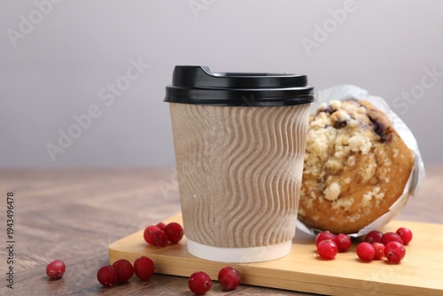 Foto Tasty muffin, coffee in takeaway cup and cranberries on wooden table against gre