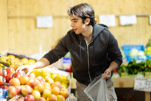 Bild auf Leinwand Man chooses ripe apples for purchase in greengrocer shop