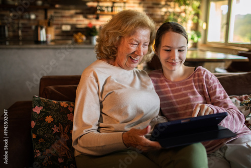 Foto Grandmother and granddaughter using a tablet at home on the sofa