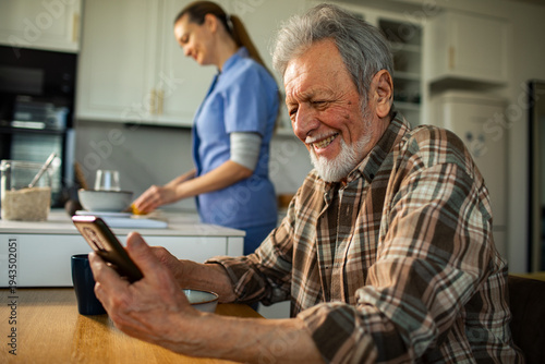 Foto Senior man using smartphone with caregiver in kitchen