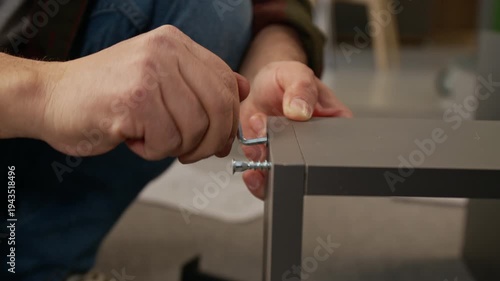 Close-up of hands of unrecognizable man driving in bolts using hex key tool, fixing together panels, while assembling flat pack locker or drawer at home