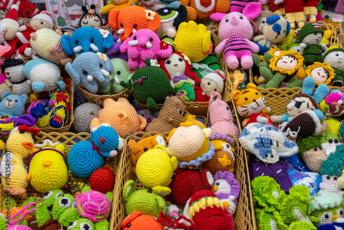 Vibrant assortment of crocheted toys featuring animals and dolls, intricately handmade and displayed on counter at handmade market. Full frame background