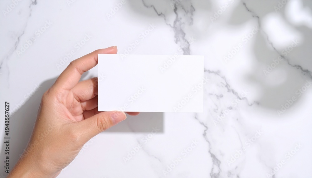 Obraz premium Hand holding a blank white business card mockup on marble background