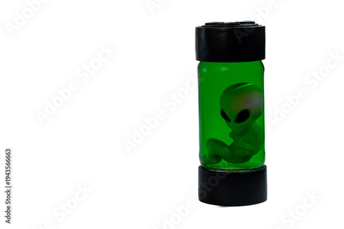 Photography Small alien figurine suspended inside a green glass jar with black end caps on white background