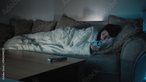 sad woman lies on the sofa in front of tv and uses the phone, have fun and enjoy