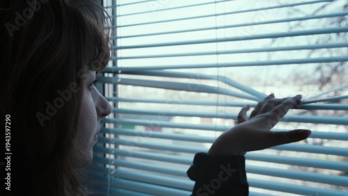 Woman looking through window blinds in a contemplative mood, A woman looks out the window attentively