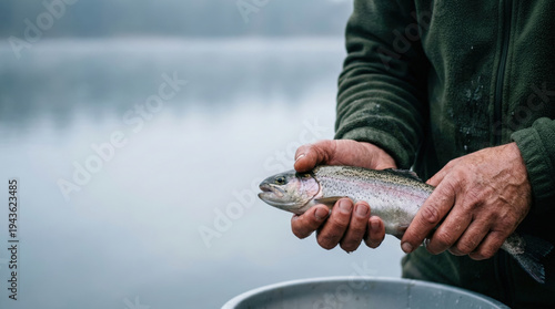 Man in Olive Green Fleece Holding Rainbow Trout by Misty Lake