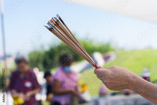 Картината върху платно Close up of a woman's hand holding burning incense sticks during the Qingming Festival at a Chinese cemetery